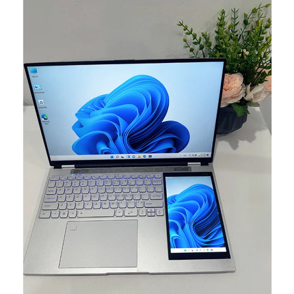 Laptop with a smaller screen attached on a white surface with a plant in the background